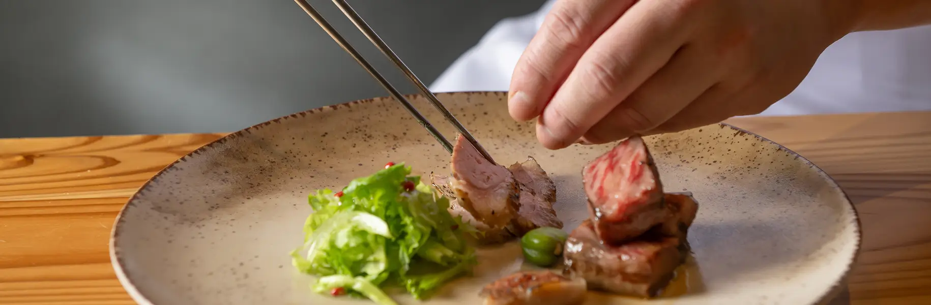 料理人が繊細な手つきで盛り付ける美味しそうな牛肉のお料理