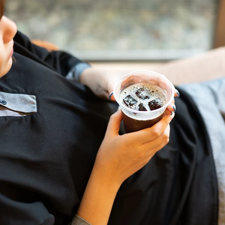 黒い館内着を着た人が、アイスドリンクを片手にくつろいでいる画像です。フリードリンクを飲みながら、リラックスした時間を過ごしている様子が伝わってきます。