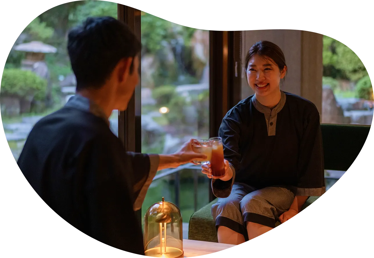 夕食後、館内着を着た男女が飲み物を片手に乾杯している画像です。窓の外には庭園が見え、2人とも笑顔でリラックスした時間を楽しんでいる様子が伝わってきます。