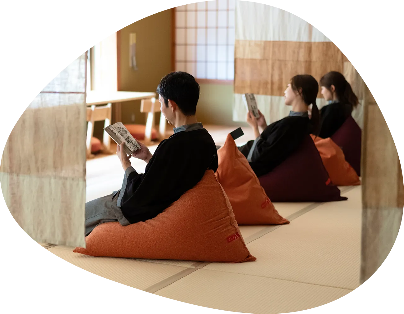 畳敷きの湯上がりどころで、3人が大きなビーズクッションに座り、それぞれ本を読んでくつろいでいる画像です。静かで落ち着いた雰囲気の中で、思い思いの時間を過ごしている様子が伝わってきます。