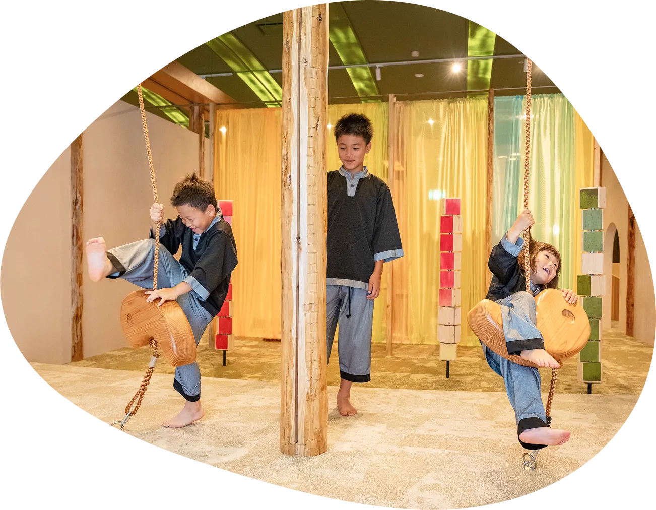 木の板でできたブランコのような遊具で遊ぶ2人の男の子と、それを見守る男の子の画像です。皆が笑顔で楽しそうに遊んでおり、子どもたちが思い切り体を動かせるキッズスペースであることが伝わってきます。